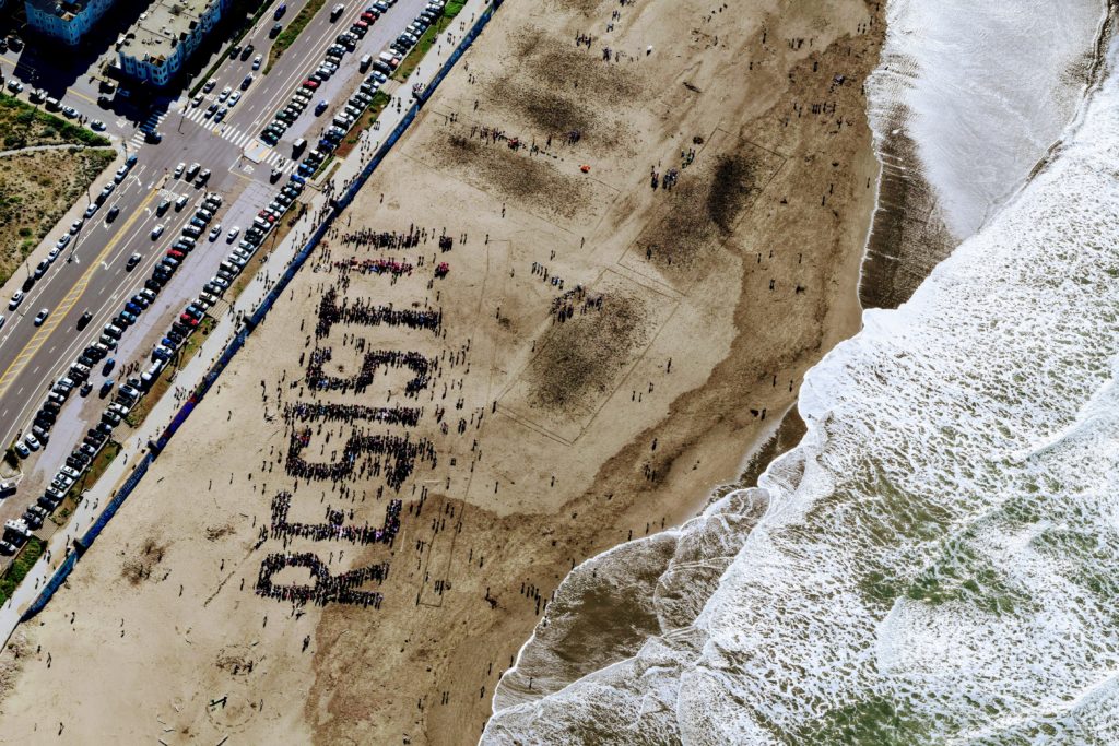 An aerial view of the beach were many people have formed the word "RESIST!!"